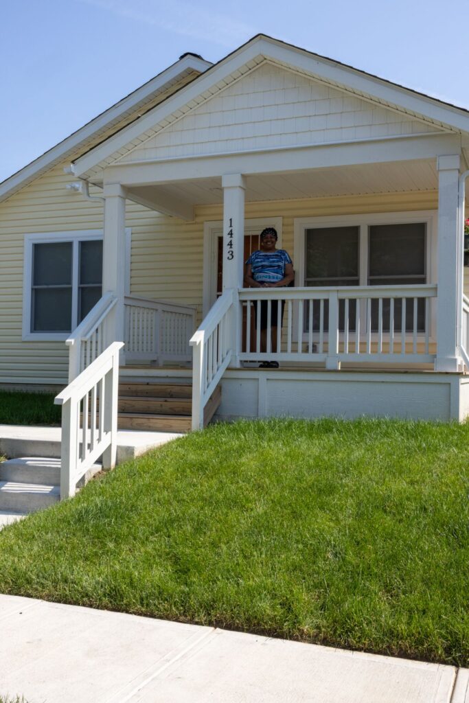 women standing on the porch of her yellow house with her hands folded